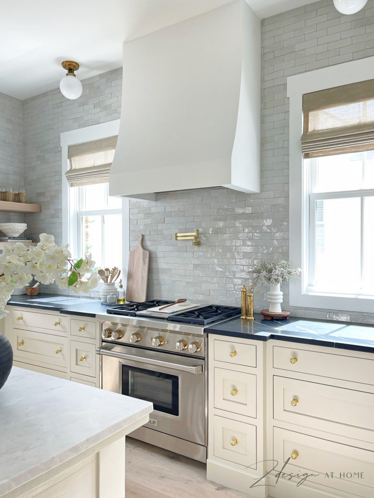 wolf range and french range hood in cottage kitchen with black marble countertops and zellige tile backsplash to ceiling