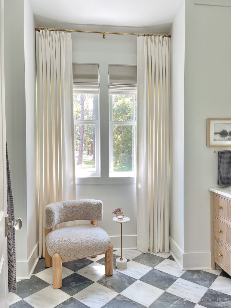 master bathroom with gray and white checkered floors, white linen curtains and linen widow shades and boucle chair