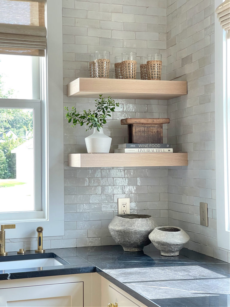 white oak kitchen shelves styled with paper mache bowls on black marble countertops