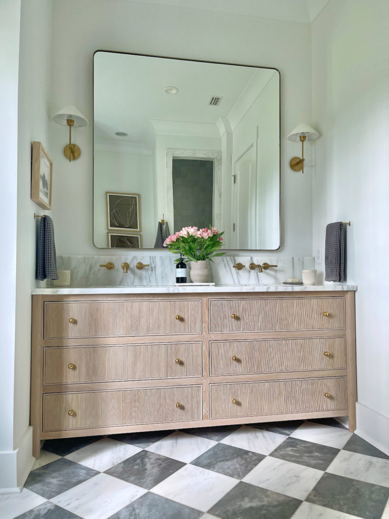 white oak reeded vanity in gorgeous bathroom with checkerboard floors and oversized brass square vanity mirror