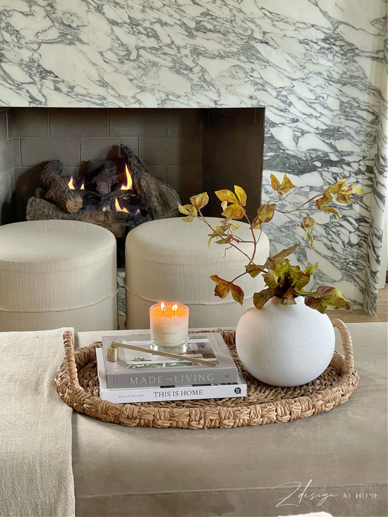 upholstered coffee table vignette with books, candle and brass candle snuffer in front of fireplace burning 